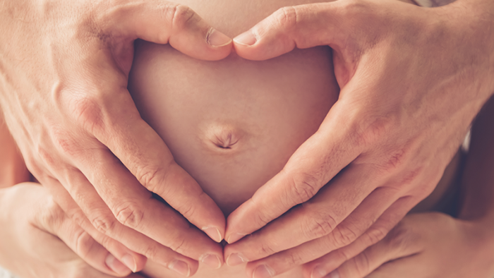 Pregnant woman gently holding her belly and smiling happily